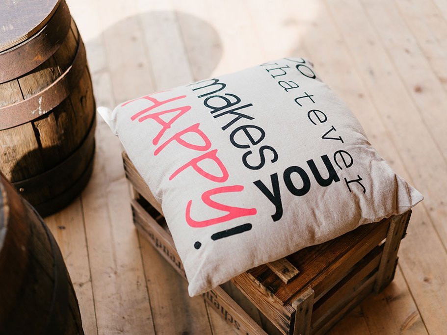 Auf einer Holzkiste liegt ein Kissen, auf dem "Do whatever makes you Happy!" steht.