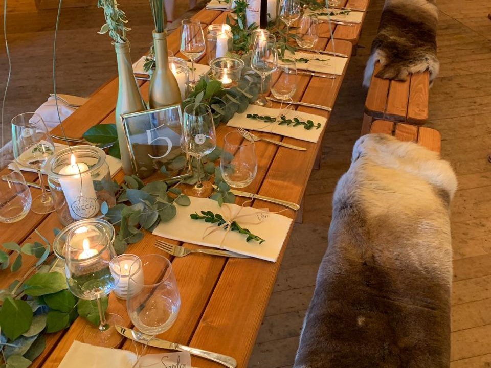 In einem Alpentipi stehen lange Tischtafeln, die mit viel Efeu, Kerzen und Geschirr dekoriert sind.